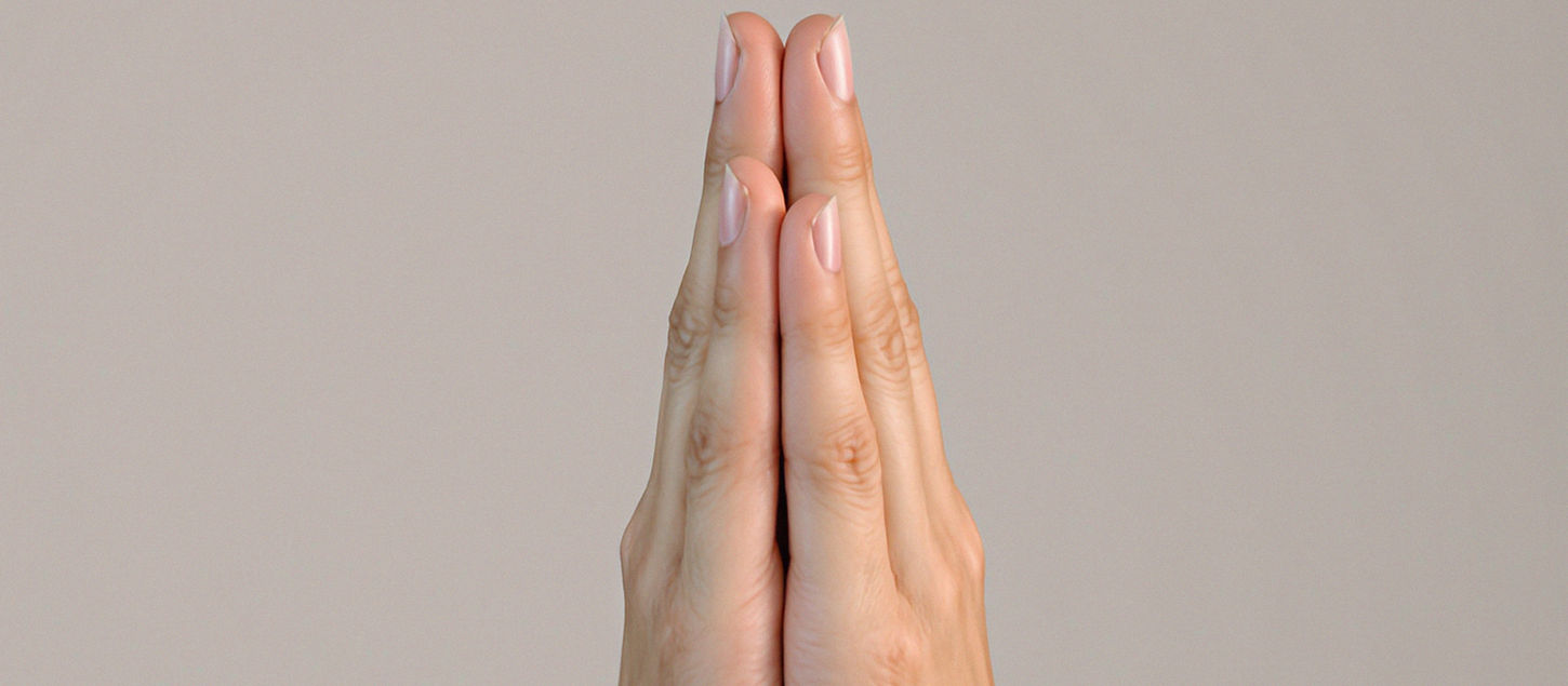 Hands clasped in prayer position against a neutral, light background.