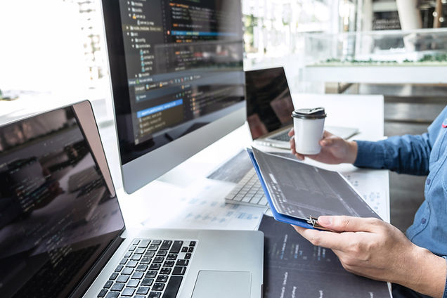 A man at work, in front of computers, reading a document and holding a coffee cup