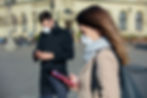 This is a picture of two people in an otherwise-empty city square, a man and a woman. Both are wearing masks and social distancing, and they're both looking at their phones. 