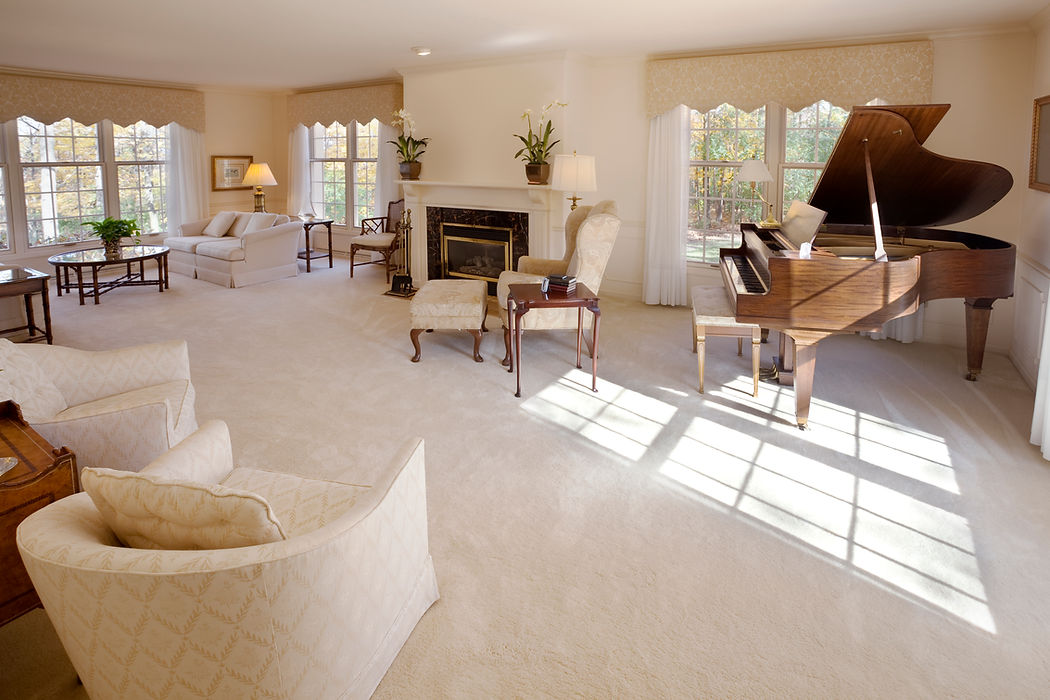 Spacious living room with a grand piano, elegant white armchairs, and a fireplace, creating a cosy atmosphere.