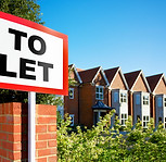 A "To Let" sign stands in front of a row of modern brick townhouses under a clear blue sky