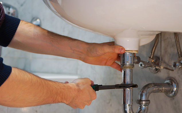 Cropped hands of a man using an orange tool to repair a pipe against a light grey wall