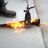 Booted worker using a torch to apply a flame to a roof
