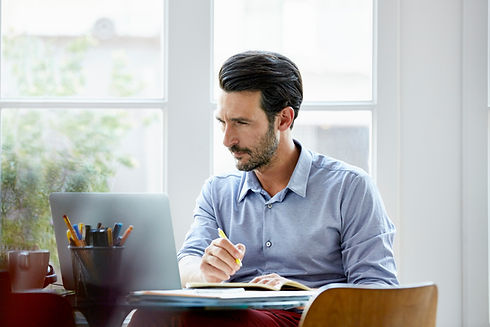 A man at a desk holding a pen and looking intently at a laptop screen