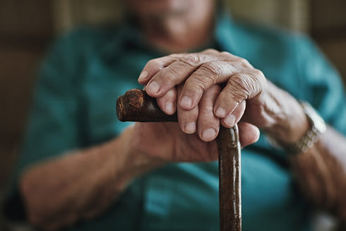 Wrinkled hands of a senior person resting on the top of a wooden cane