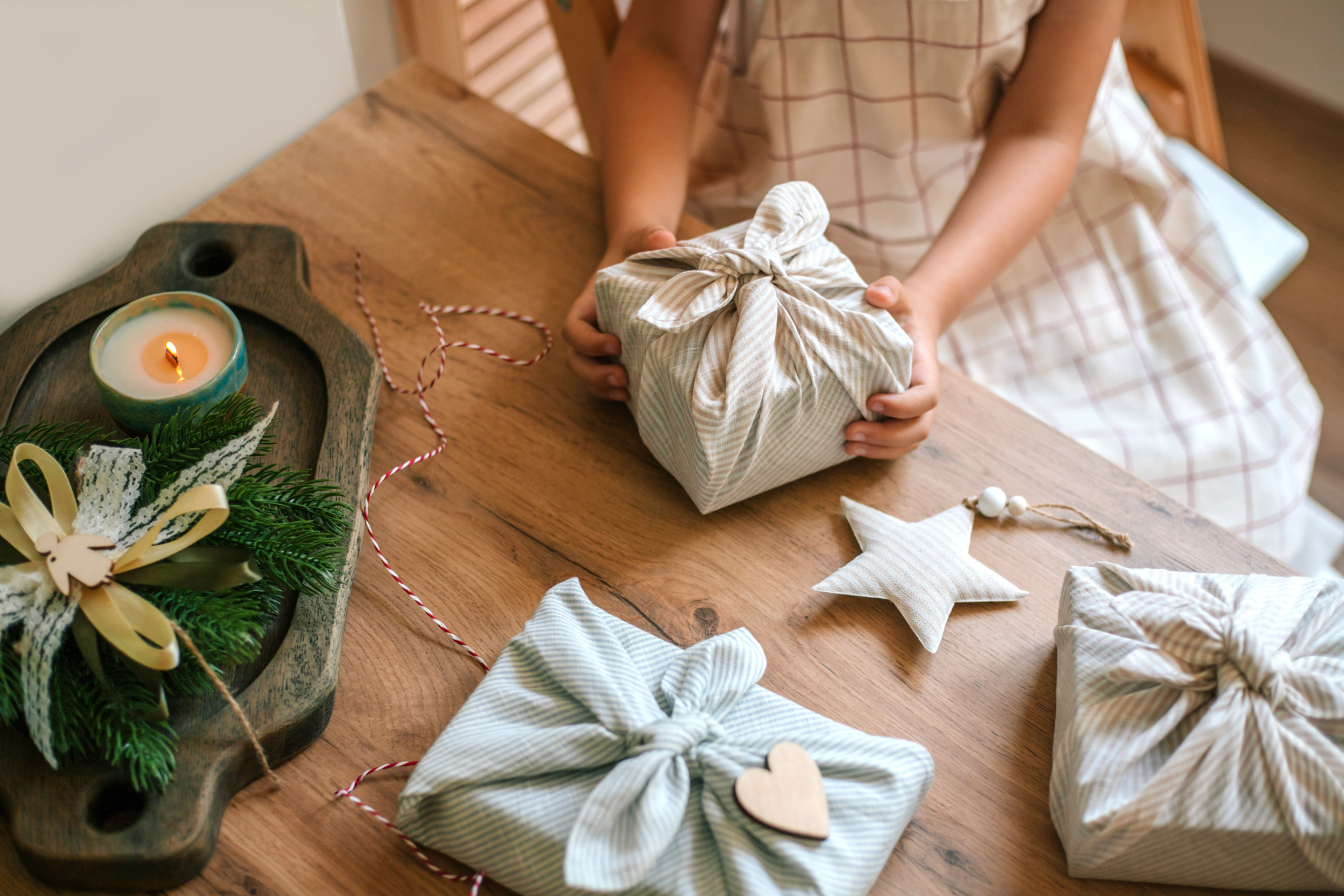 A close-up shows hands unwrapping a gift wrapped in reusable cloth on a wooden table, highlighting sustainable gift-giving.