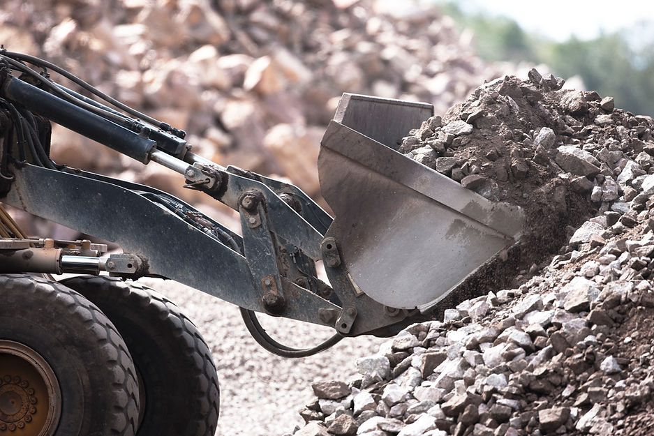 Close-up of a blue front-end loader bucket scooping textured gravel or wood chips