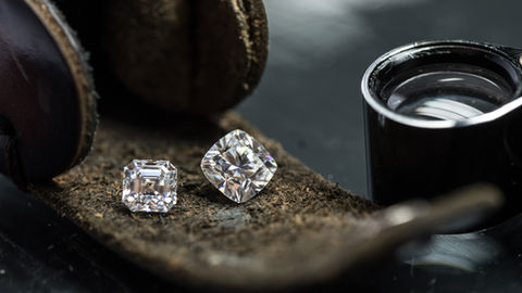 Deux diamants taillés reposent sur un tissu sombre, vus à la loupe, avec reflets brillants.