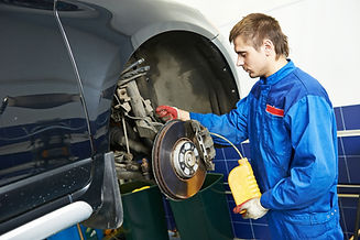Car mechanic working on the brake disc and suspension of a lifted motor vehicle