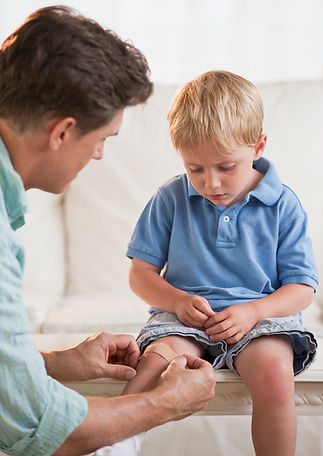 A man gently places a bandage on a young boy's knee
