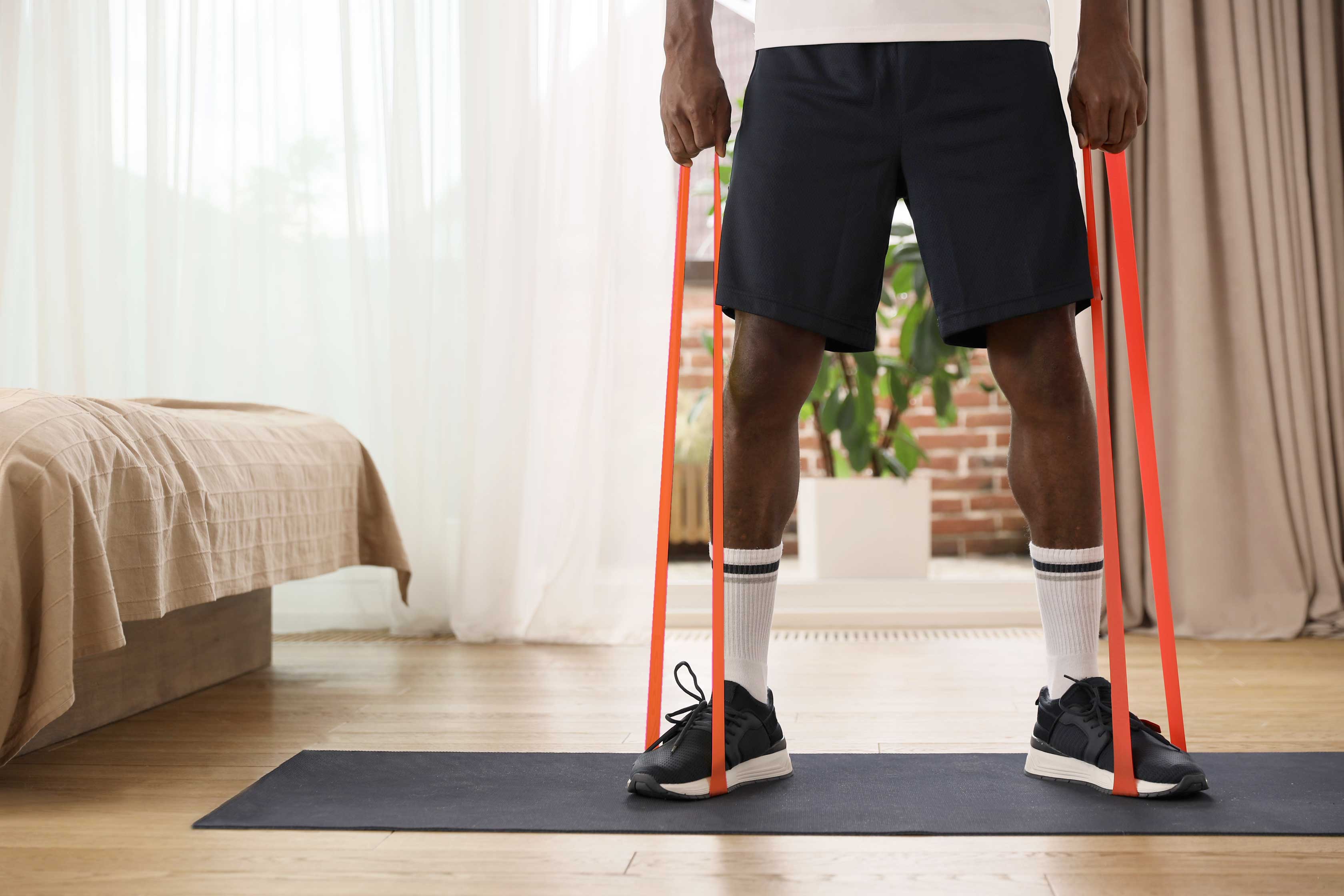 Person standing on a yoga mat using resistance bands in a well-lit room.
