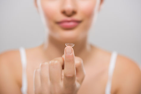Focus on contact lens on finger of young woman. Young woman holding contact lens on finger