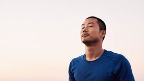 An Asian man meditating with his eyes closed.