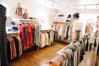 Interior of small clothing shop with white walls and rails of women's clothing for sale