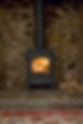 A wood stove with a visible fire set against a rustic stone wall