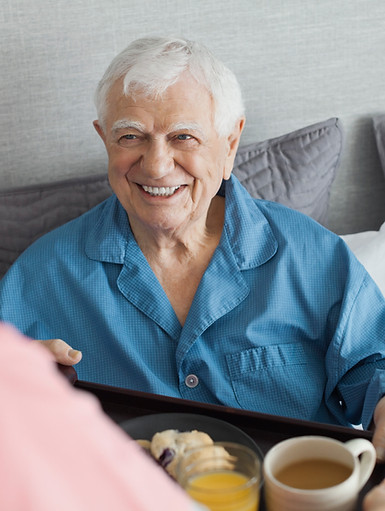 A person serving breakfast to a senior man