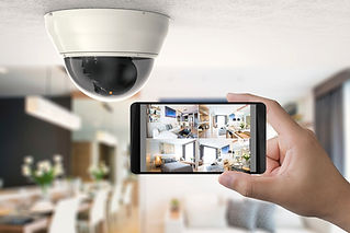A hand holds a smartphone showing security footage from a dome camera mounted on a ceiling