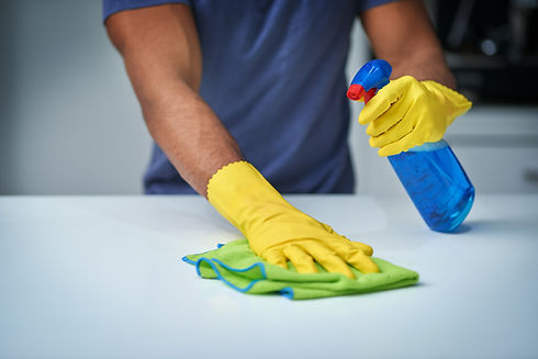 Person cleaning a white surface with a green cloth and blue spray bottle
