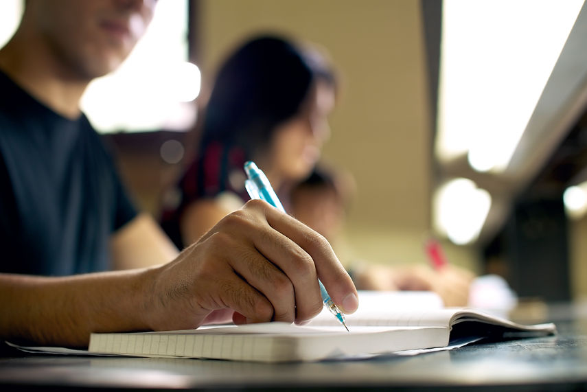 Students doing homework and preparing exam at university, closeup of young man writing in