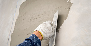 Close up of plasterer applying wet grey cement plaster to wall using metal trowel