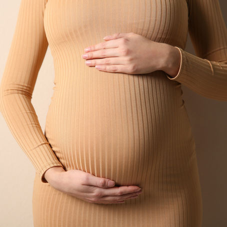 A woman in a tan dress holding her hands on her baby bump