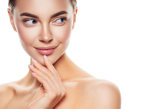 A woman with glowing skin and subtle makeup touches her chin, smiling softly
