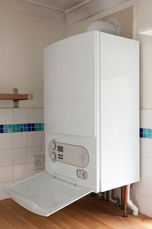 Wall-mounted boiler with open front panel revealing controls, set against white tiled wall and wooden counter