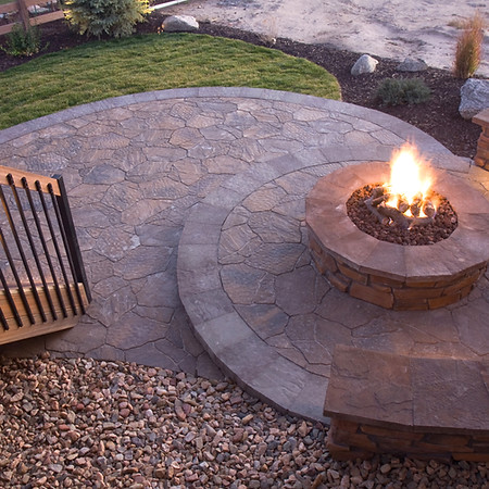An elevated view of a circular flagstone patio with a lit fire pit in the centre