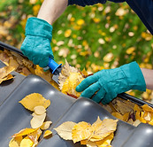 A man taking autumn leaves out of gutters