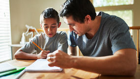 A man helping a school-age boy with homework.