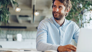 An IT professional sitting comfortably at his desk, smiling and engaging in a friendly conversation with a colleague, reflecting a positive, relaxed, and fulfilling workplace environment.