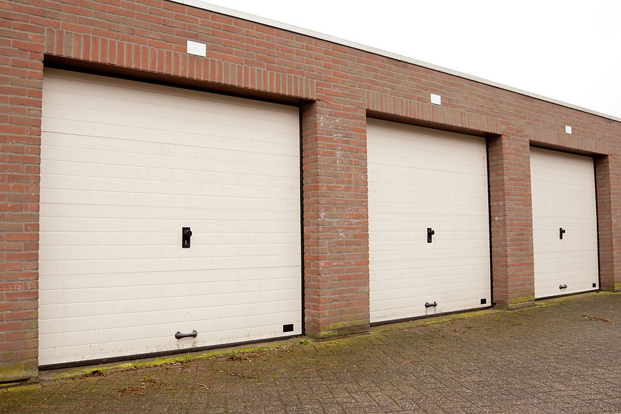 Three closed white garage doors set in a brick wall, casting soft shadows on a paved driveway
