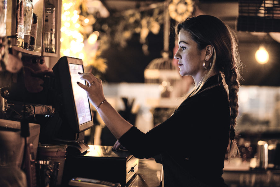 Female bartender serving drinks at a bar, working behind the counter under warm lighting.