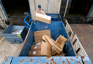 Worker throws empty cardboard boxes into an industrial trash compactor, part of the process