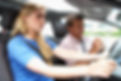 Young female learner driving as male instructor takes notes on clipboard