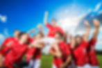 A joyful soccer team in red jerseys celebrates under a bright blue sky