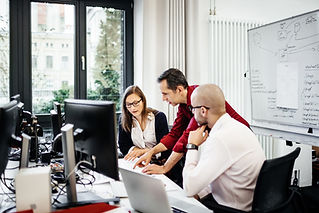 Three colleagues, two men and a woman, collaborate around a desk with computers.