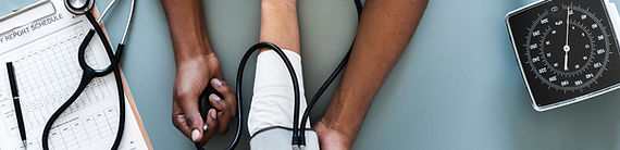 A doctor in a white coat is taking the blood pressure of a patient while a nurse is holding the patient's arm.