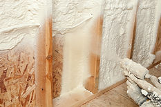 Construction worker applying spray foam insulation to wall studs