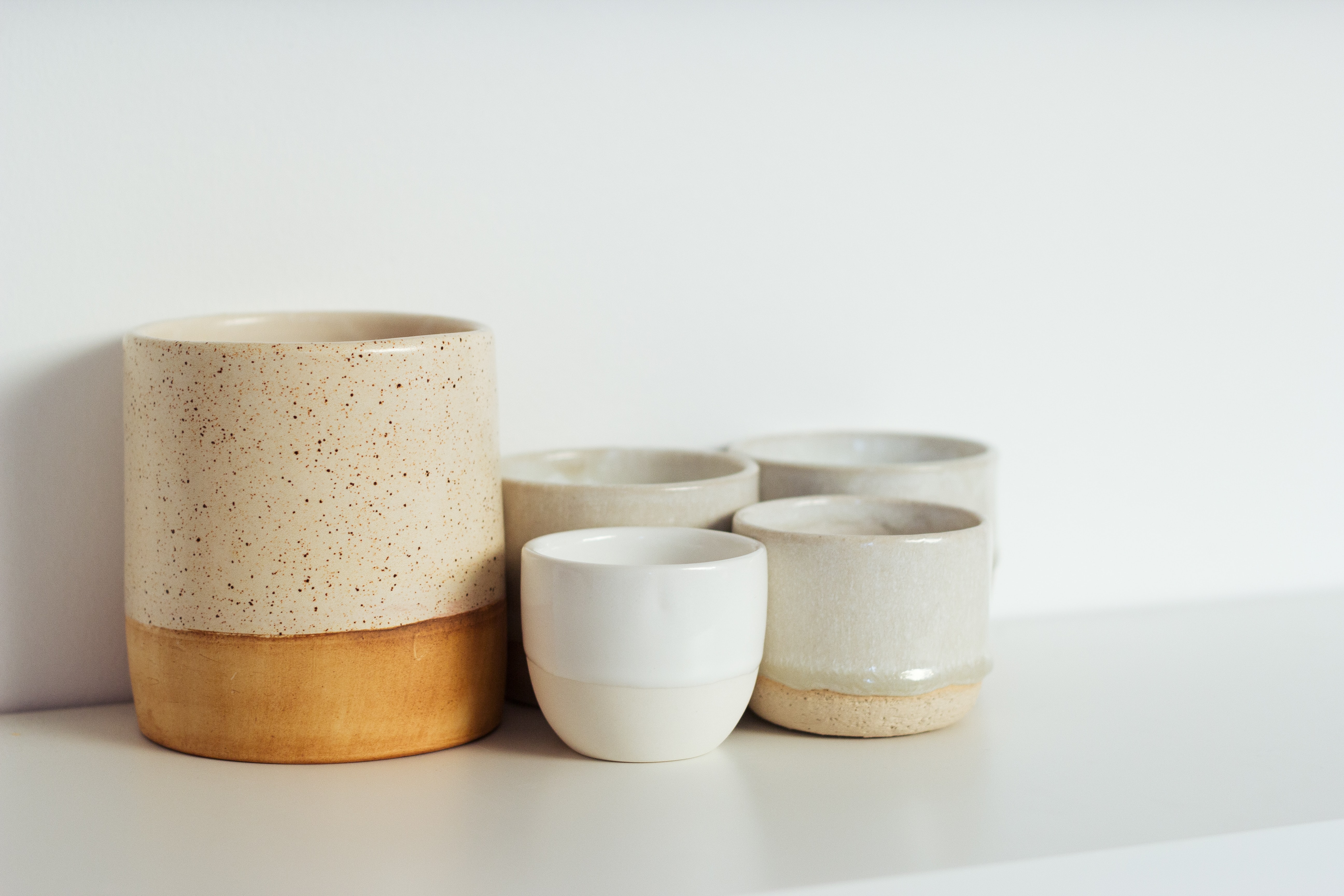 A set of ceramic cups and bowls with neutral colors arranged on a clean white shelf.