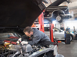Mechanic using a flashlight to work on the engine under an open car hood