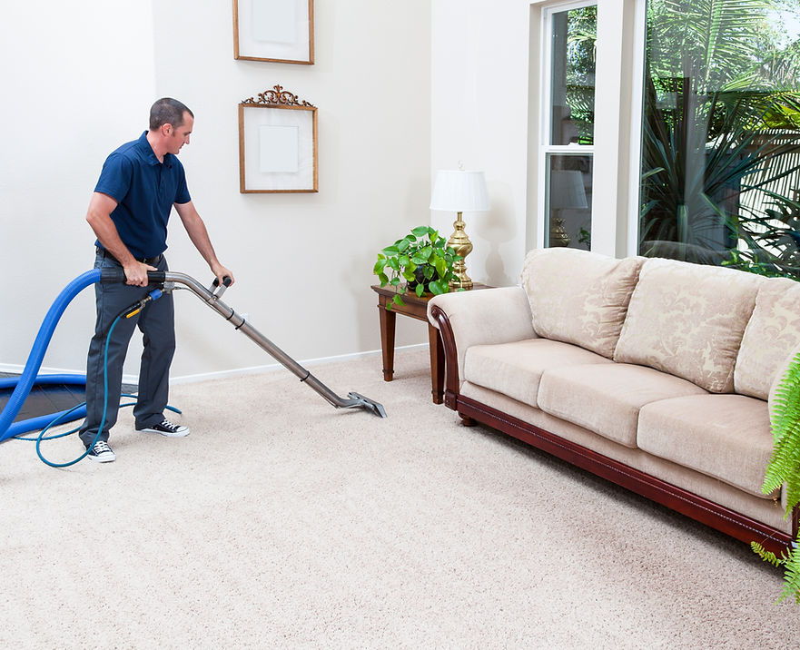 Cleaner using a hot water extraction hose tool to deep clean a large beige fabric corner sofa