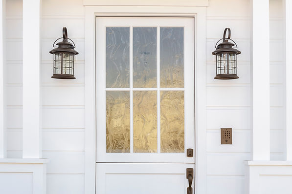 Close-up of a white panelled door with six panes of textured glass and two dark metal lanterns