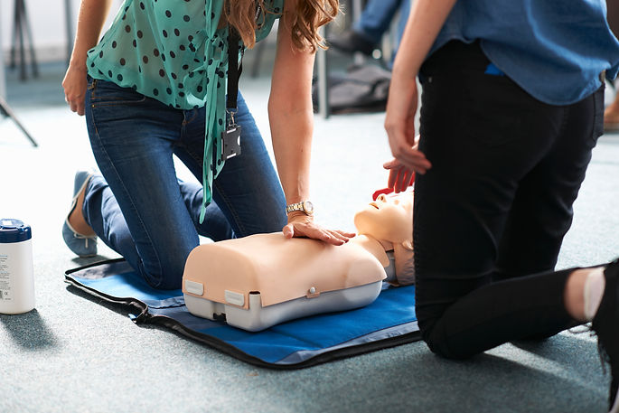 Two people kneel on the floor, practicing CPR on a training dummy