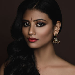 Mulher com bindi tradicional, brincos jhumka e maquiagem.