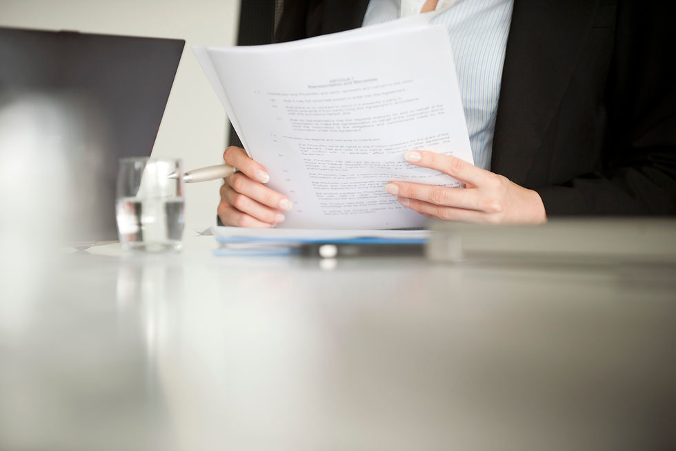 A close-up of a professional in business attire holding and reading paper documents at a desk.