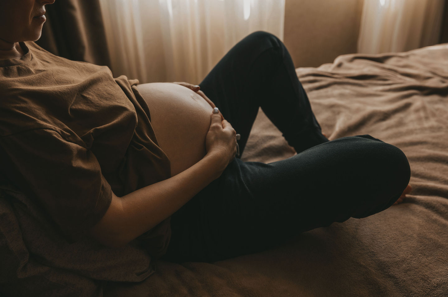 Maternity Photography by Blake Ferguson depicts a woman holding her Baby Bump in bed with warm, relaxing tones in Ontario, Canada.