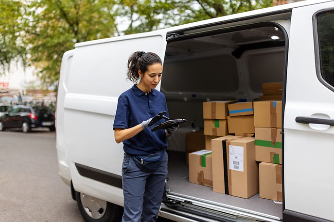 Delivery person using digital tablet while standing by delivery van. Female courier worker