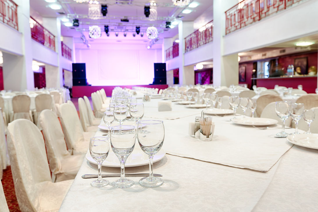 Elegantly set banquet hall with rows of white-covered tables and chairs, wine glasses, and plates
