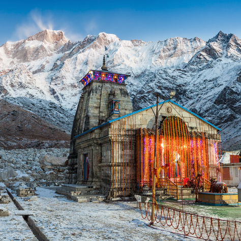 Snow-covered Kedarnath Temple surrounded by icy mountains during winter season with clear blue sky.